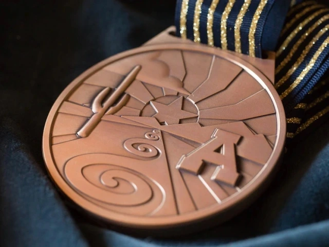 Bronze medal with geometric panels, stylized letter A and swirl motifs, attached to a blue-and-gold striped ribbon on dark fabric.