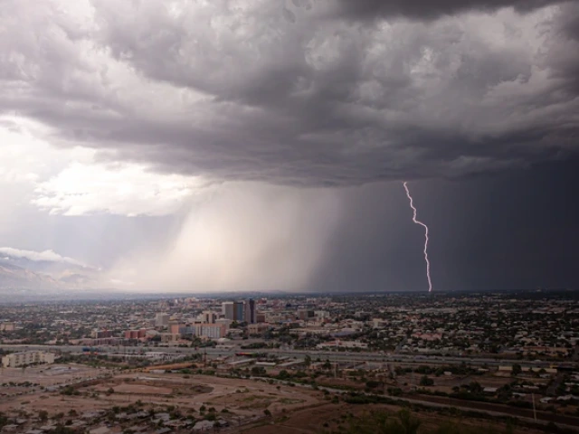 A large storm cloud hovers over a Southwestern metropolitan area. In the distance, rain falls as a bolt of lightning flashes.