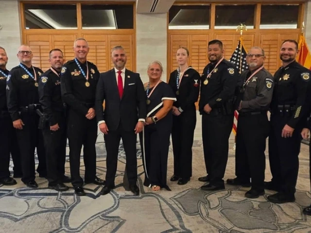 A group of University of Arizona Police Department officers stand in a line with U.S. Rep. Juan Ciscomani at the Veteran Servant Leader Award ceremony. The officers wear formal uniforms and medals, and U.S. and Arizona flags are displayed behind them.